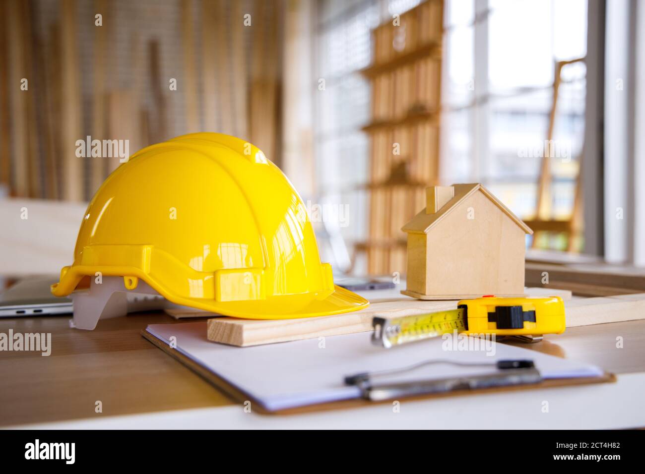 Gelber Schutzhelm, winziges Holzhaus und Maßband auf Tischlertisch. Stockfoto