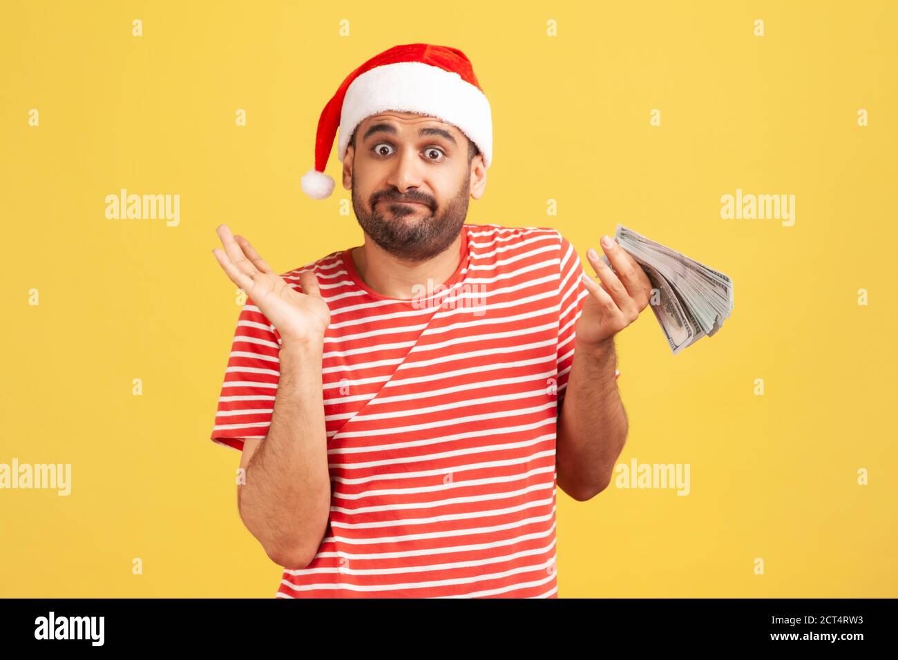 Verwirrt verwirrt Mann mit Bart in roten weihnachtsmann Hut hält Geld in den Händen, nicht wissen, wie man seine Zulage, Urlaub Vergünstigungen verbringen. Innenaufnahme im Studio Stockfoto