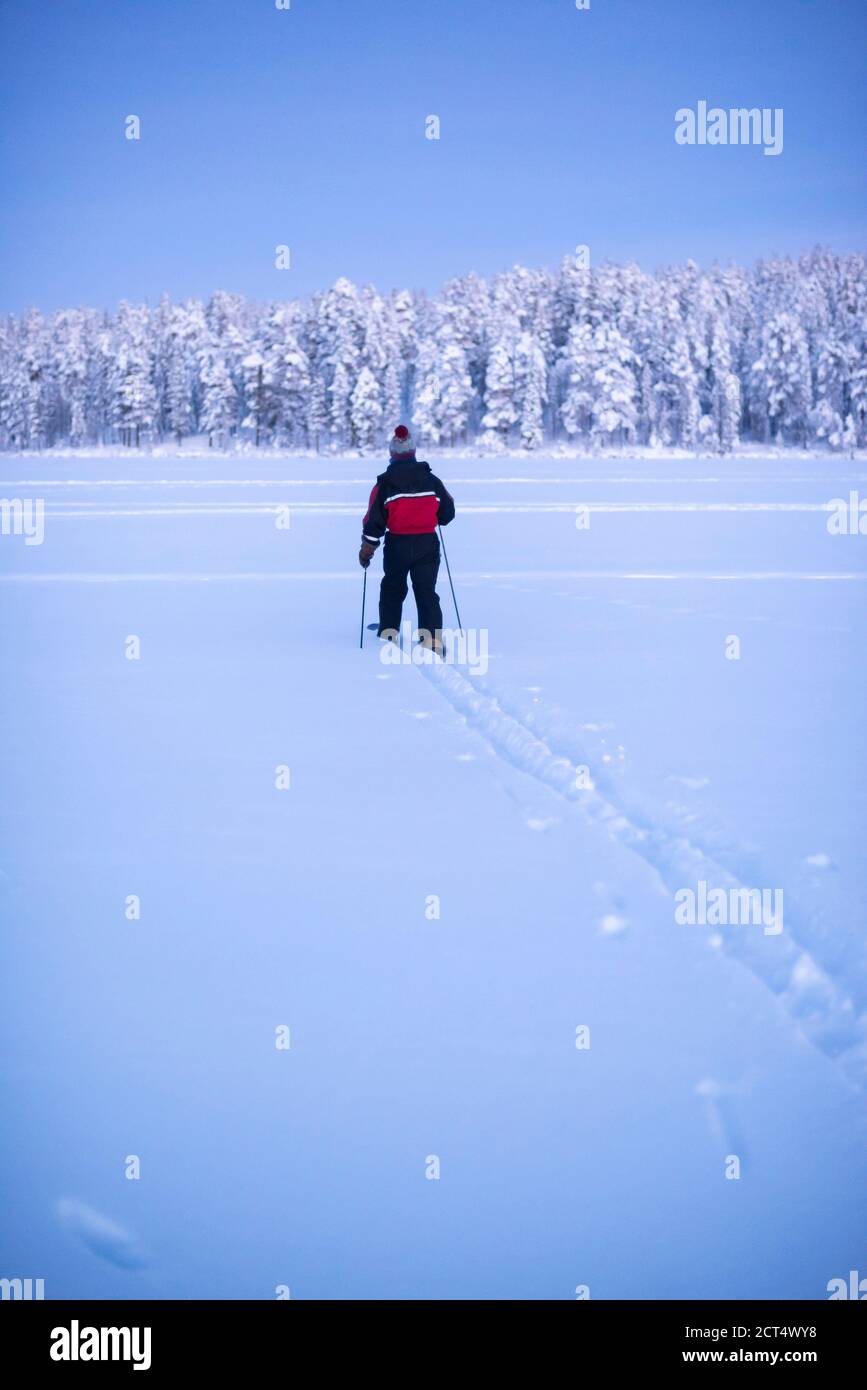 Ein Mann auf einem einsamen abgelegenen Skiabenteuer auf dem gefrorenen See in Torassieppi bei Sonnenuntergang in einer Winterlandschaft, Lappland, Finnland Stockfoto