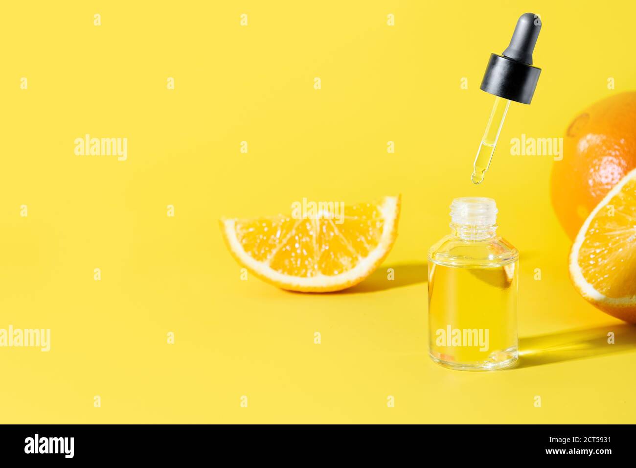 Kosmetische Hyaluronsäure oder feuchtigkeitsspendende Öl- und Orangenessenz in Glasflasche mit fliegender Pipette auf gelbem Hintergrund mit Kopierraum für Design. Stockfoto
