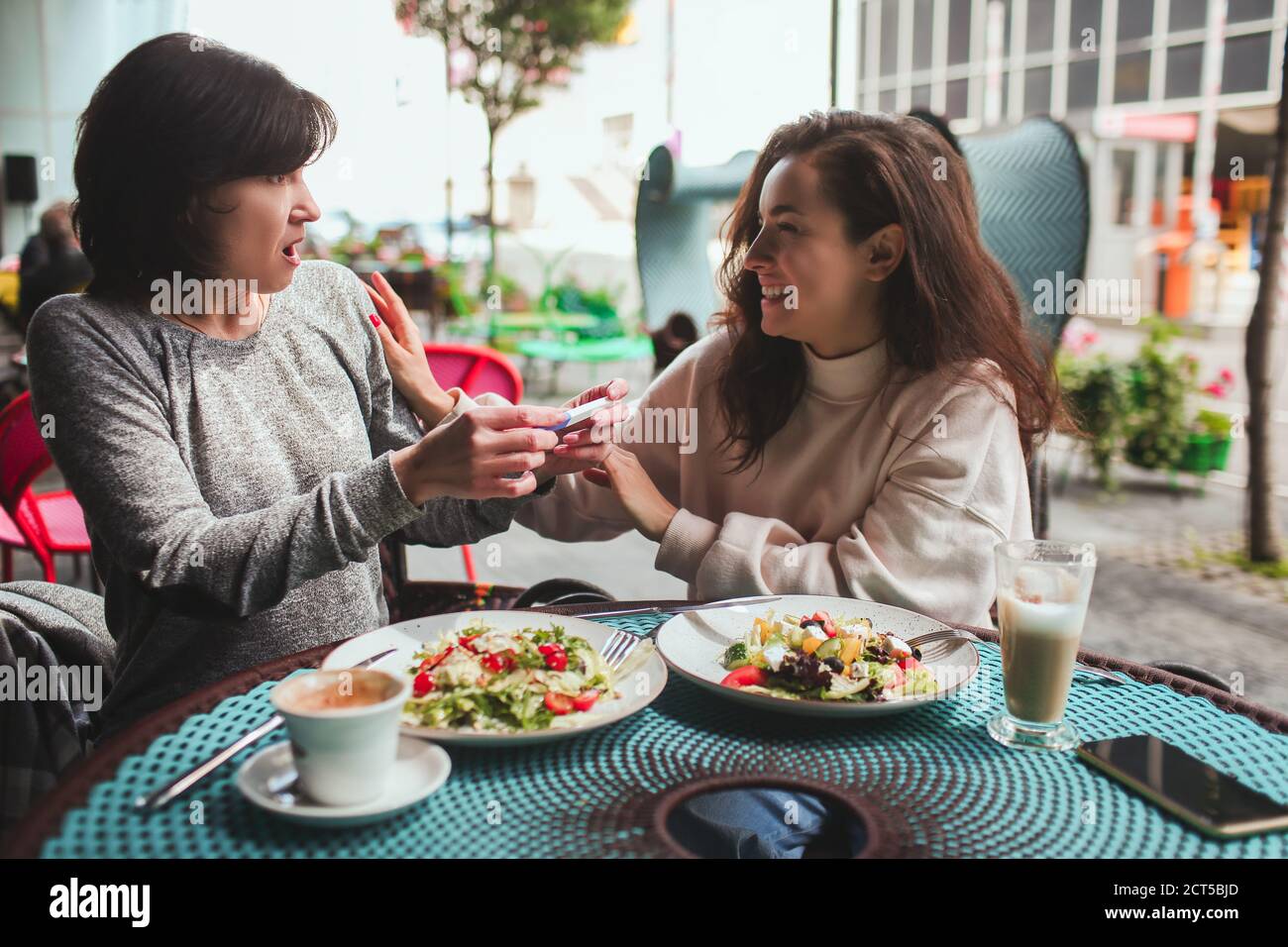 Die reife Mutter und ihre junge Tochter sitzen zusammen im Café oder Restaurant. Schockierte reife Frau, die von der Schwangerschaft ihrer Tochter hörte. Beide Stockfoto