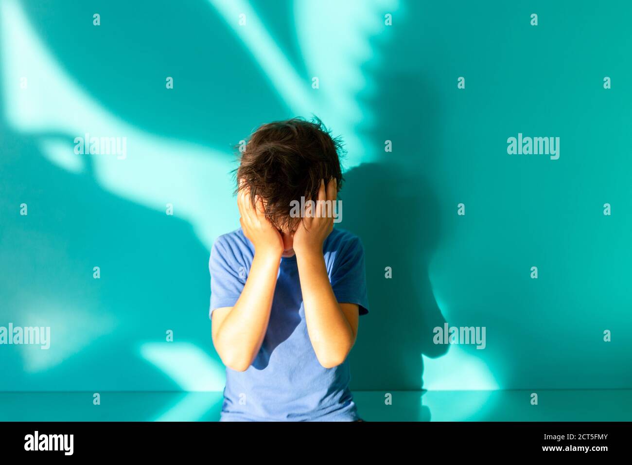 Portrait eines traurigen oder frustrierten Brünetten Jungen in einem blauen Hemd. Daumen hoch. Türkisfarbener Hintergrund mit Schatten. Bildung. Blick und Lächeln auf die Kamera Stockfoto