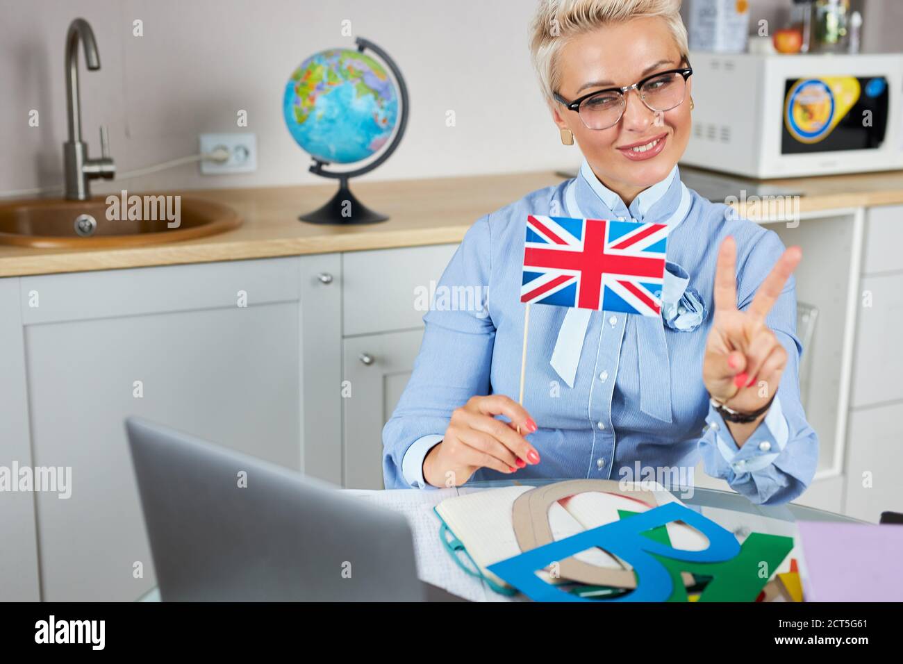 Cool modernen englischlehrer Online-Unterricht über Webcam auf Laptop halten, sieht sie auf Bildschirm lächelnd, großbritannien Flagge in den Händen Stockfoto