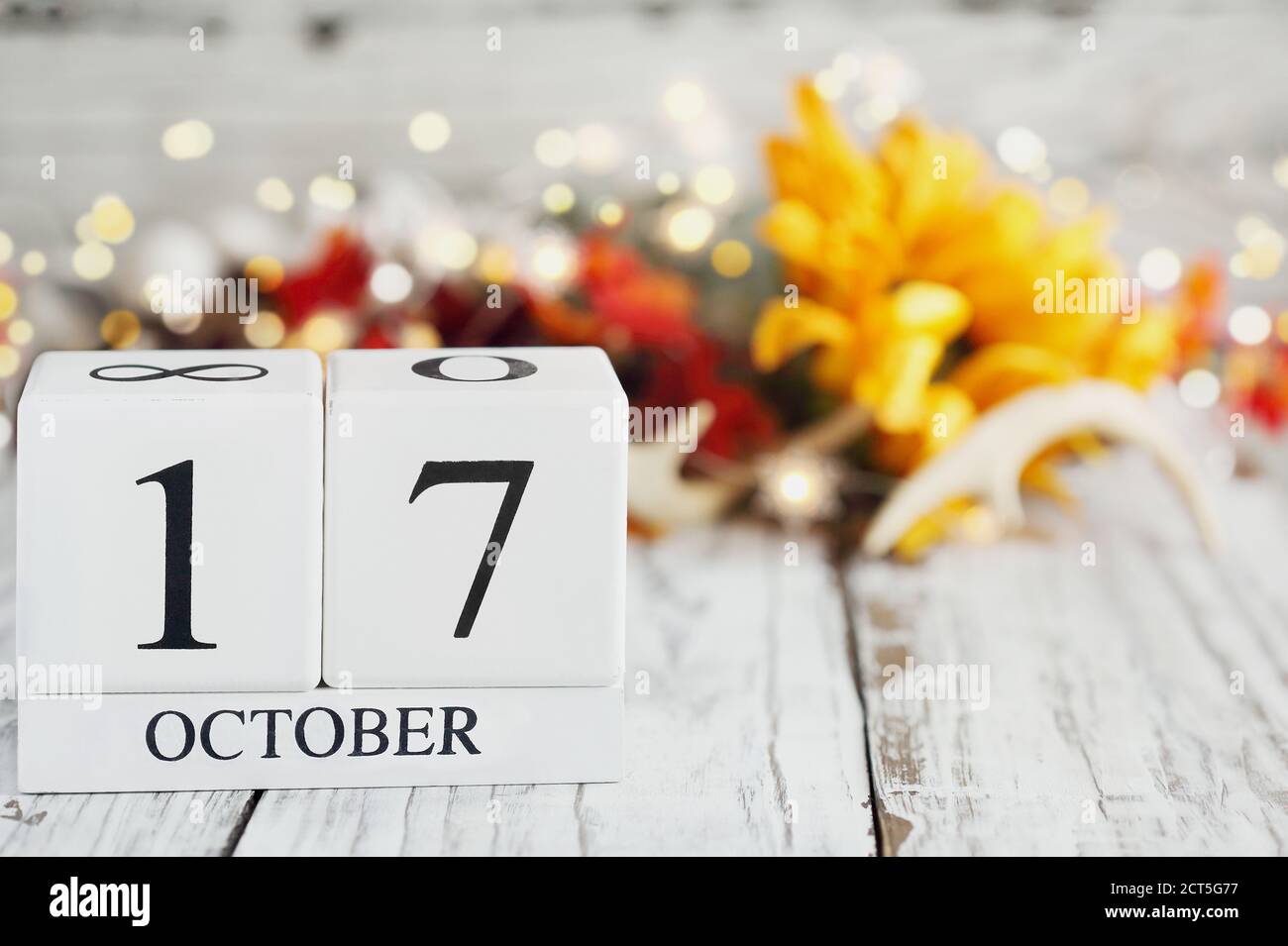 Weiße Holzkalenderblöcke mit dem Datum vom 17. Oktober und Herbstdekorationen über einem Holztisch. Selektiver Fokus mit unscharfem Hintergrund. Stockfoto