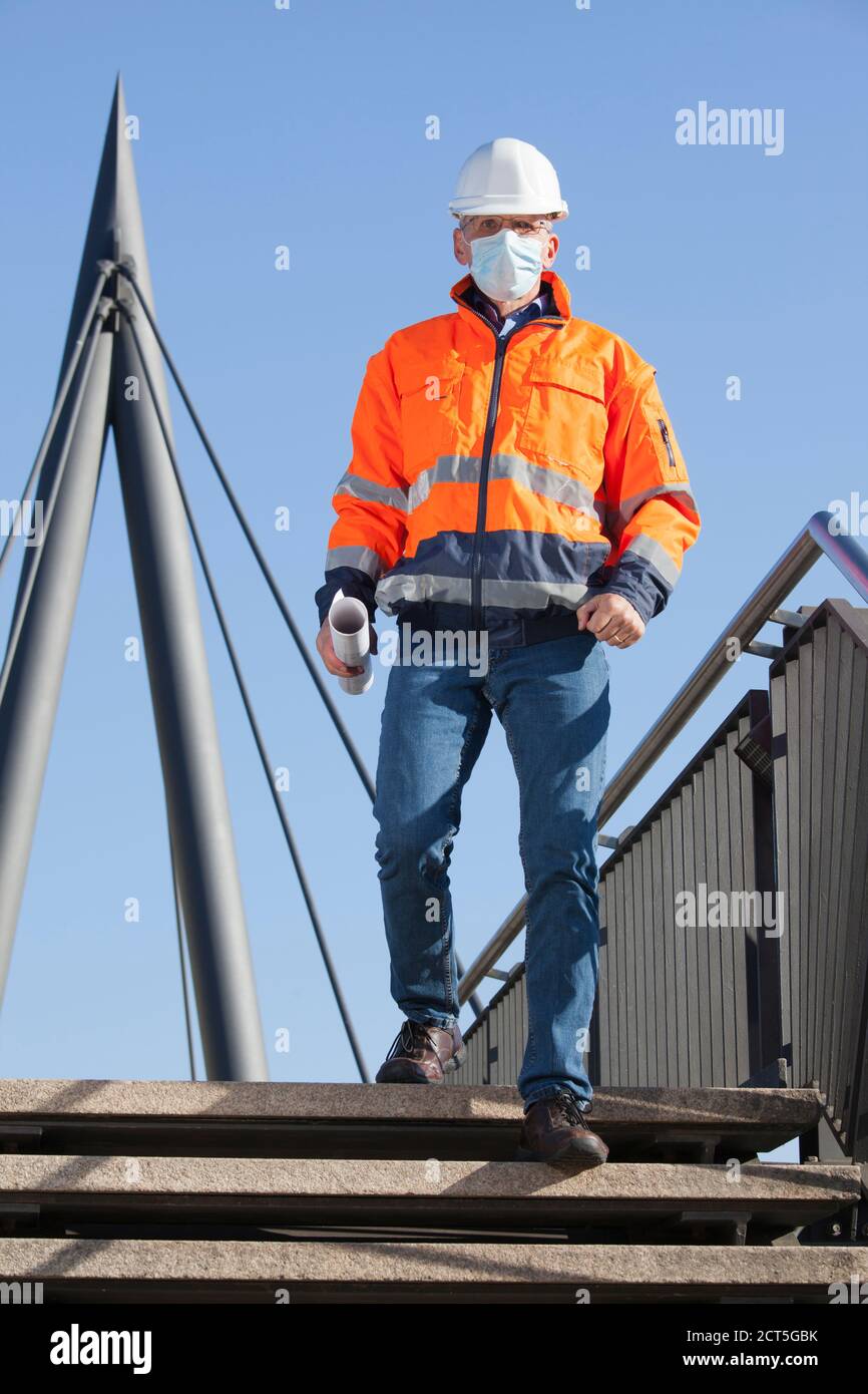 Architekt oder Ingenieur mit Gesichtsmaske und Schutzkleidung zu Fuß Unten - konzentrieren Sie sich auf das Gesicht Stockfoto