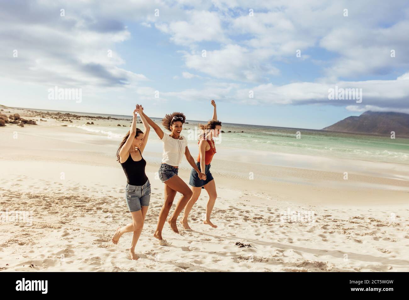 Drei Freundinnen genießen gemeinsam am Strand. Freunde tanzen am Strand zusammen und halten die Hände. Stockfoto