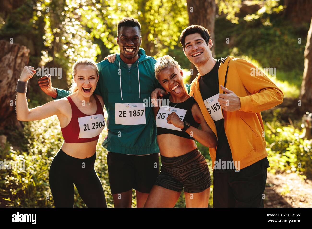Team von Läufern feiert nach dem Gewinn des Rennens. Glückliche Marathonläufer stehen nach einem Rennen im Wald zusammen. Stockfoto