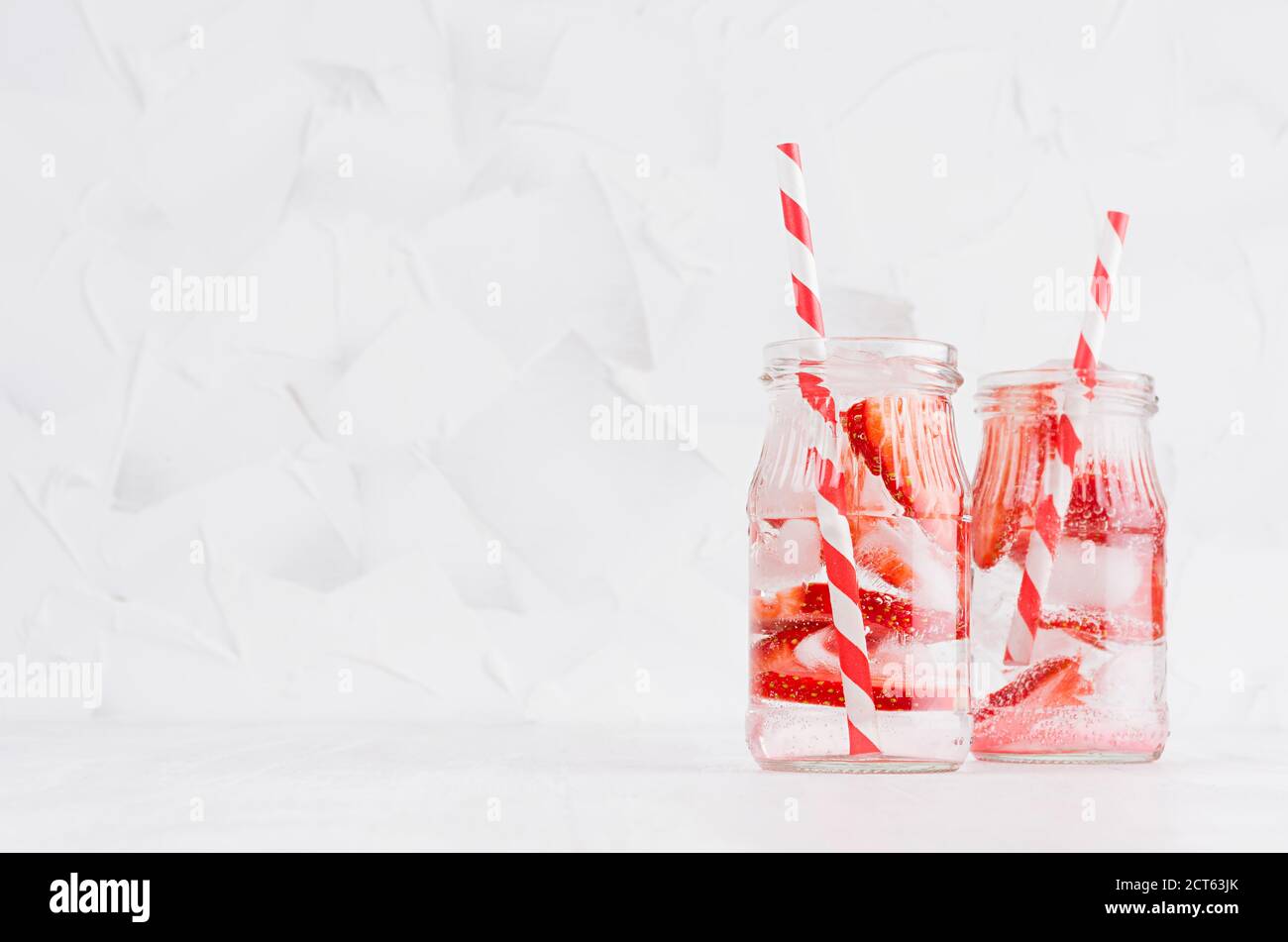 Joy helle frische Sommergetränke mit roten Erdbeeren, Stroh, Eis, Sodawasser in eleganten Gläsern auf weichen hellen weißen Holztisch, Kopierraum. Stockfoto