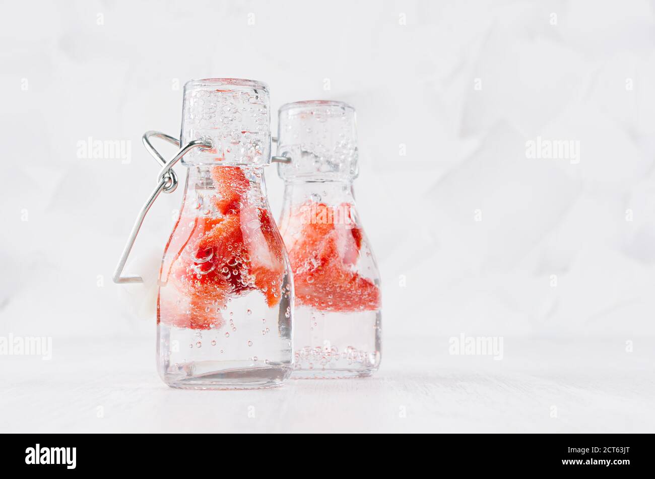 Natürliche Bio-Cocktails mit Erdbeere, kohlensäurehaltiges Wasser in zwei Yoke-Flaschen auf hellweißem Holzbrett und Wand, Kopierraum. Stockfoto