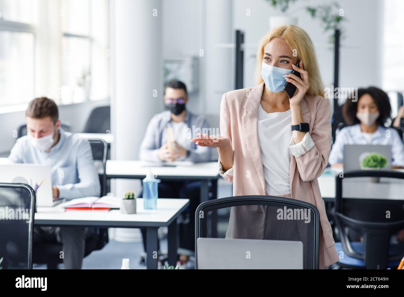 Junge Leute wieder bei der Arbeit im Büro nach der Sperre. Geschäftsfrau in Schutzmaske spricht am Telefon mit Client Stockfoto