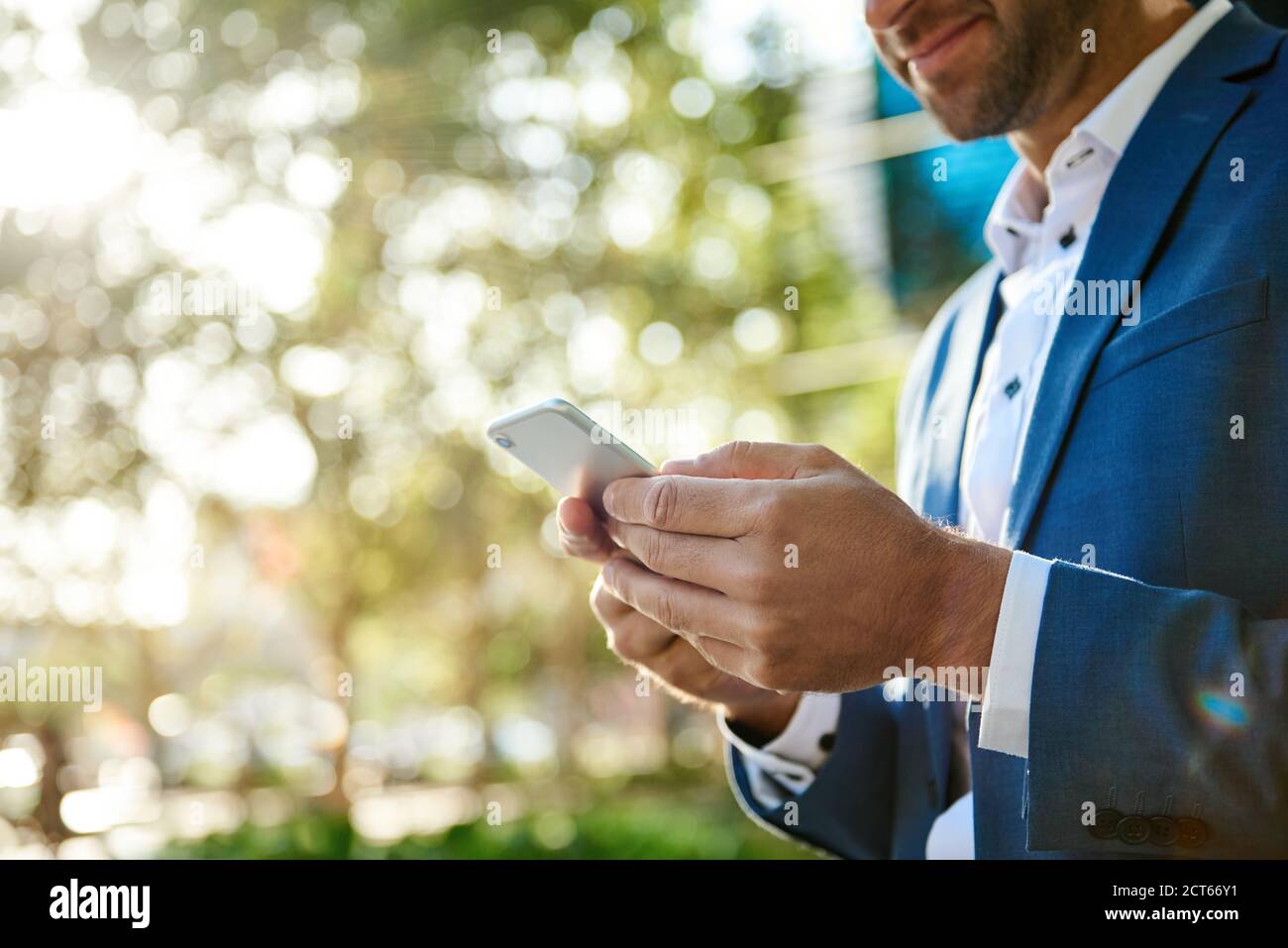 Lächelnder Geschäftsmann, der draußen steht und einen Text auf seinem Handy sendet Stockfoto