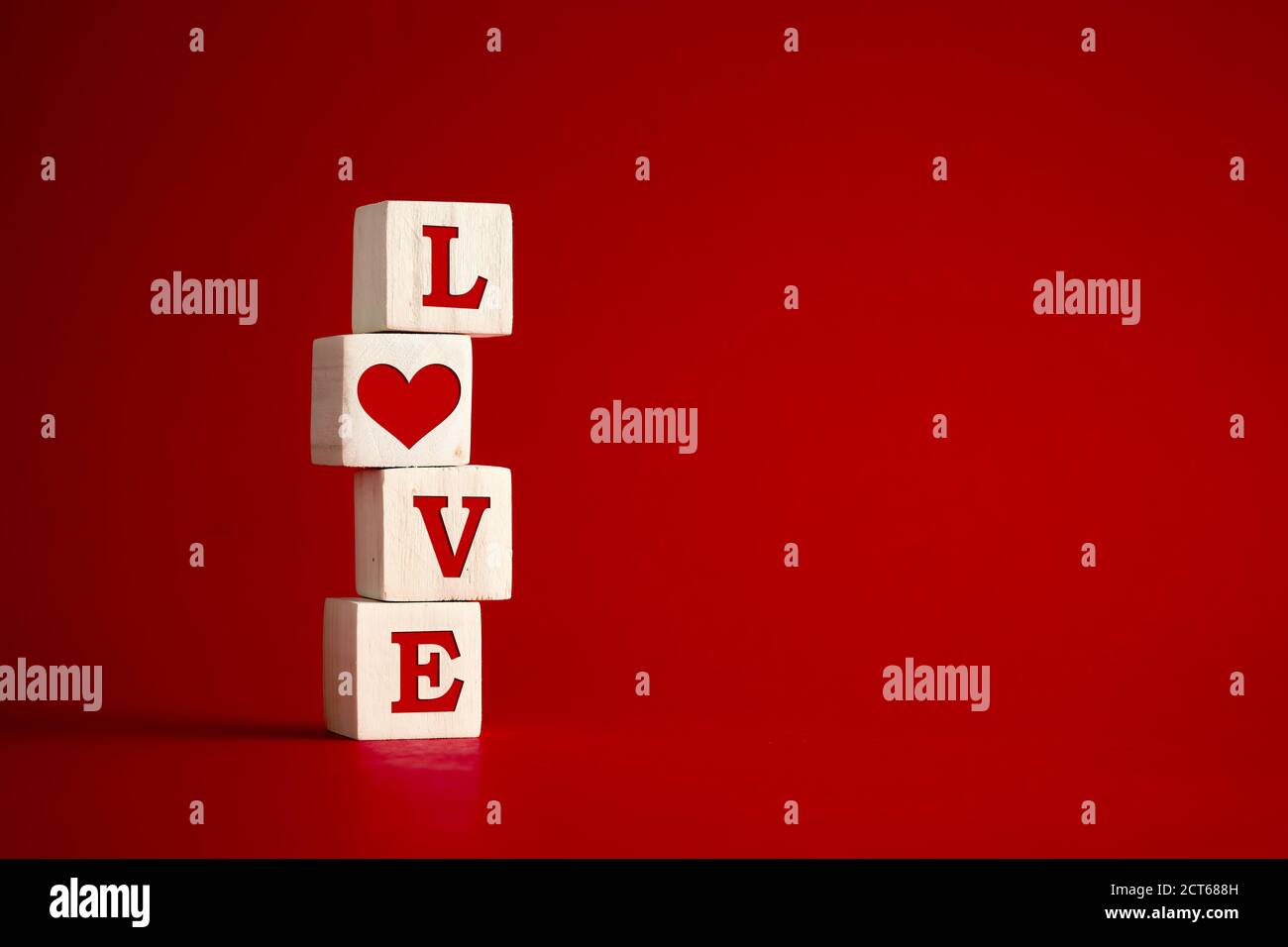 Das Wort Liebe mit Herzform auf Holzwürfeln vor rotem Hintergrund. Liebe, Romantik, Beziehung oder Valentinstag Konzept. Stockfoto
