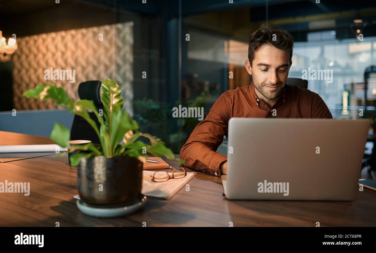 Geschäftsmann, der außerhalb der Geschäftszeiten in einem Büro mit einem Laptop arbeitet Stockfoto