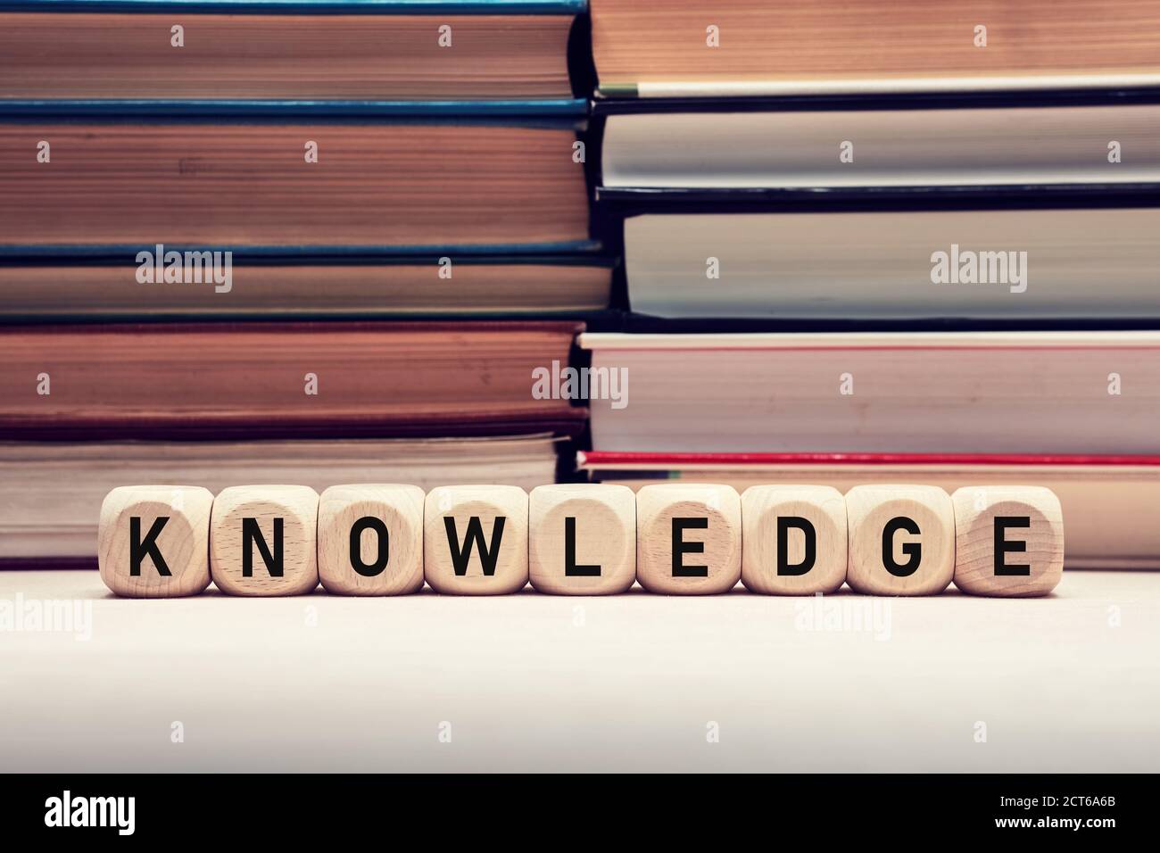 Das Wort Wissen auf Holzwürfel vor gestapelten Büchern Hintergrund. Bildung, Weisheit und Lernkonzept. Stockfoto