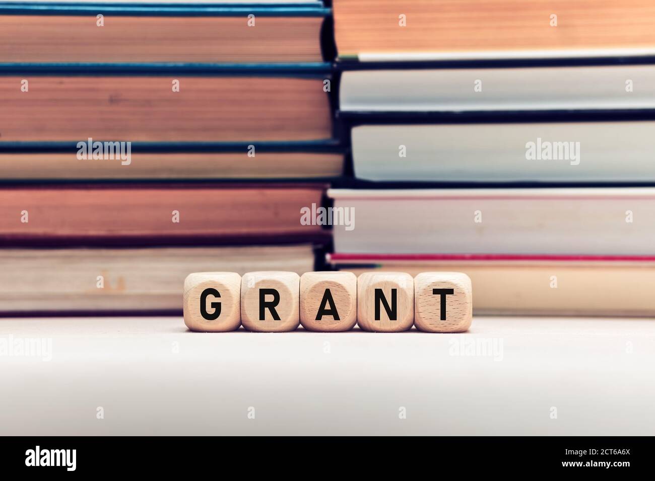 Das Wort Grant auf Holzwürfel vor gestapelten Büchern Hintergrund. Konzept der Förderung von Bildung oder Forschung. Stockfoto