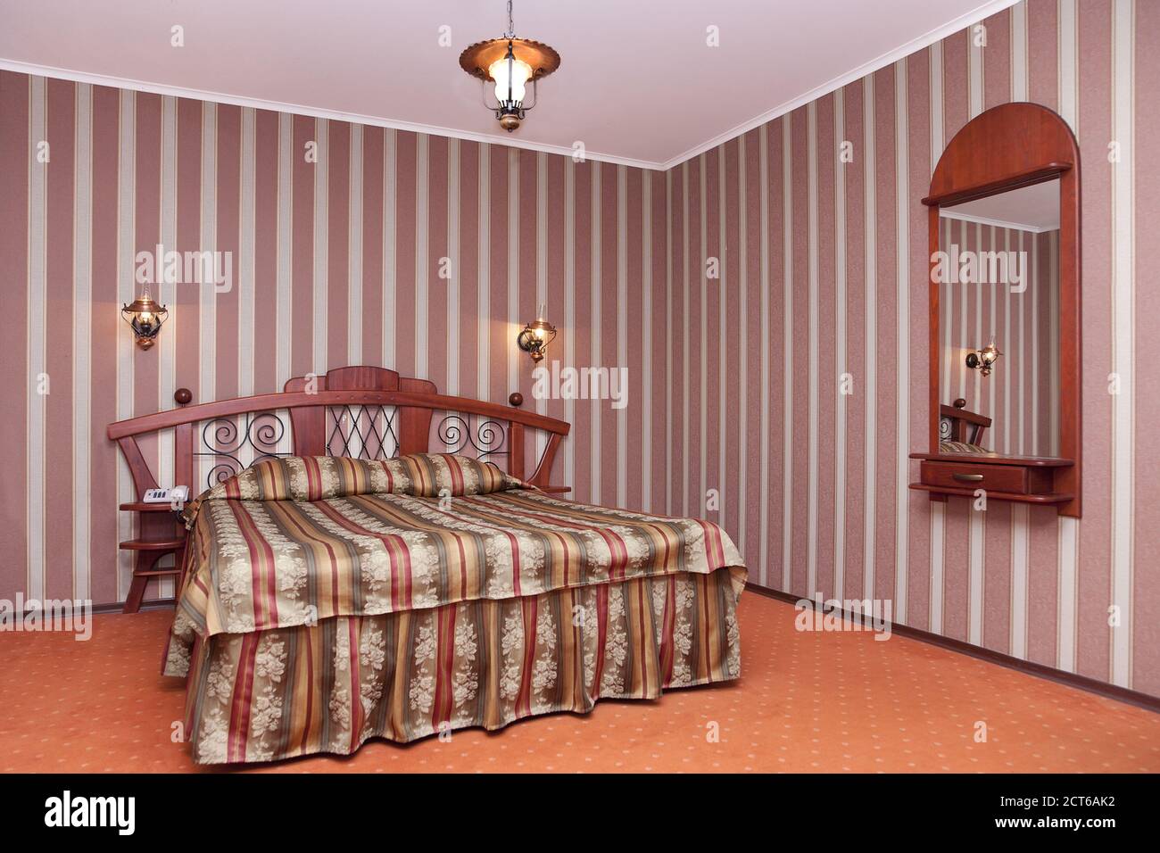 Ein Hotel mit altmodischen Zimmern im Retro-Stil, einem Schlafzimmer mit karierter Bettwäsche, gestreifter Tapete und Spiegel. Stockfoto