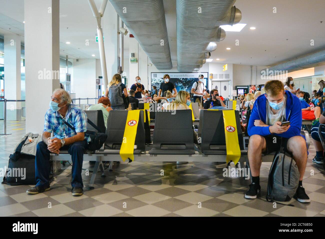Ein alter und ein junger Passagier mit Coronavirus-Schutzmasken sitzen und warten auf die soziale Distanzierung am Terminal des Flughafens Pisa, Italien Stockfoto