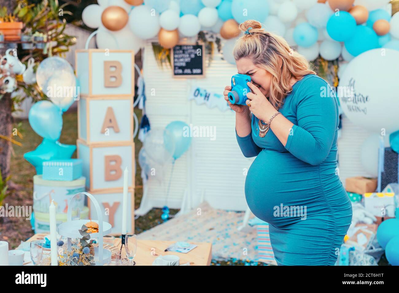 Schwangere Frau, die Fotos von einem dekorierten Tisch für Baby-Dusche. Fotokamera, Party Dekorationen in weiß und blau Farben, Baby Junge Stockfoto