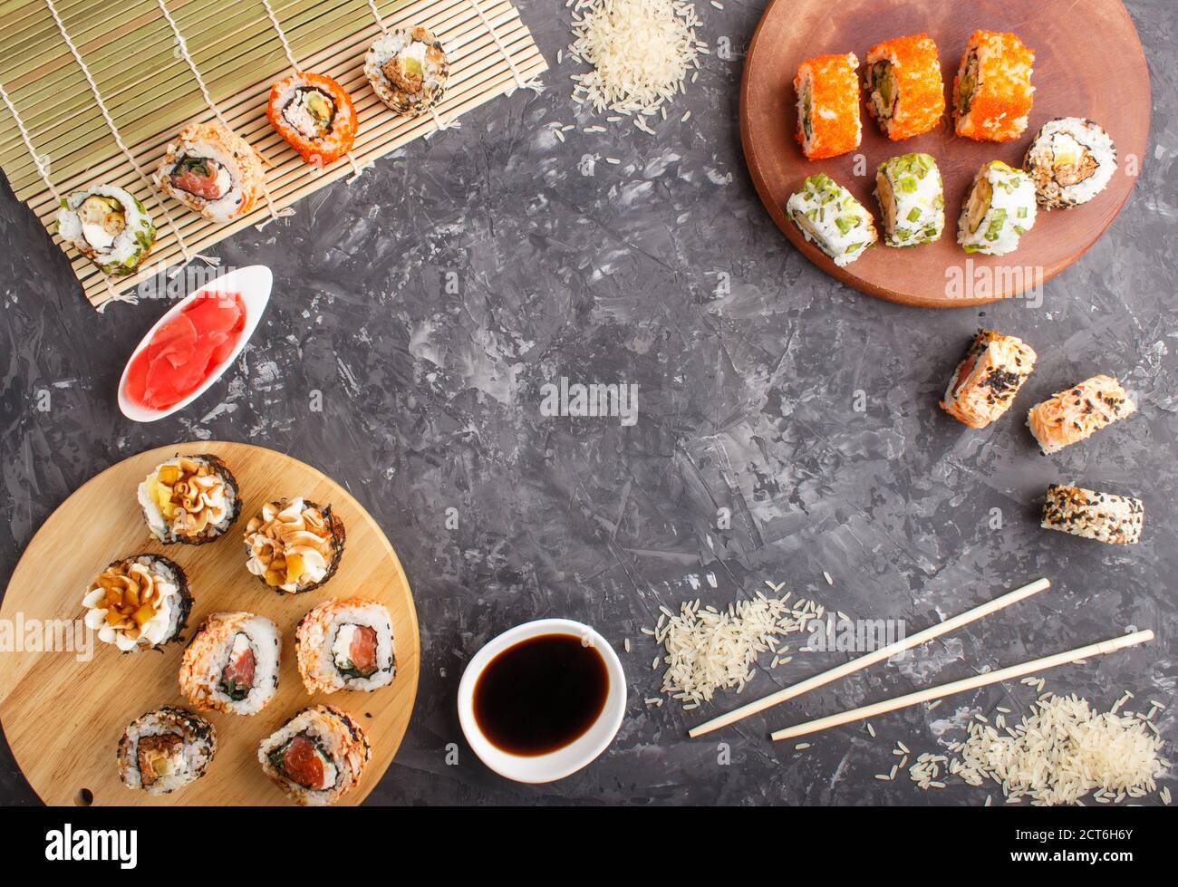Verschiedene Arten von japanischen Maki Sushi-Rollen mit Lachs, Sesam, Käse, Rogen und Essstäbchen, Sojasauce, mariniertem Ingwer auf einem schwarzen Beton Backgrou Stockfoto