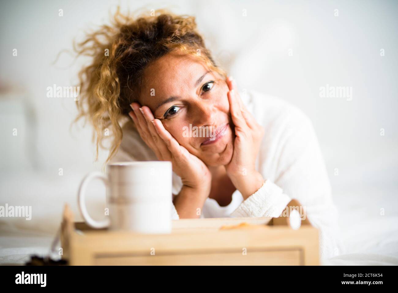 Fröhliche schöne junge Erwachsene kaukasischen Frau Porträt legte sich in Das Schlafzimmer auf dem Bett mit einer Tasse Tee oder Kaffee - glücklich peole zu Hause genießen Sie die m Stockfoto