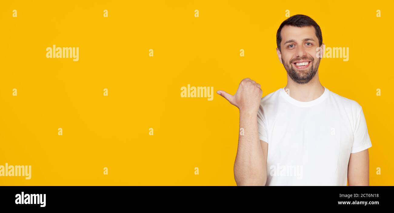 Junger Mann mit Bart in weißem T-Shirt glückliches Gesicht lächelnd mit glücklichem Gesicht suchen und zeigen auf die Seite mit Daumen nach oben. Steht auf isoliertem gelben Hintergrund. Stockfoto