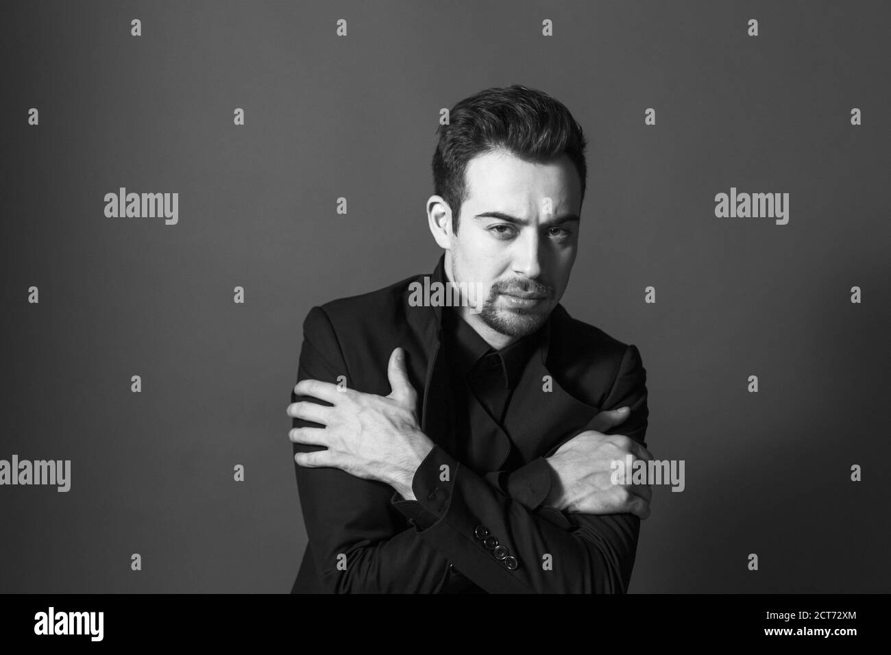 Nahaufnahme Porträt eines jungen schönen Mannes in einem Anzug, Arme gekreuzt auf der Brust, Blick auf die Kamera, vor schlichten Studio-Hintergrund Stockfoto