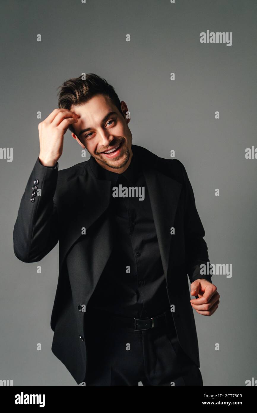 Jungen gutaussehenden Mann in einem schwarzen Anzug, Lachen, und wenn man die Kamera, gegen normales studio Hintergrund Stockfoto