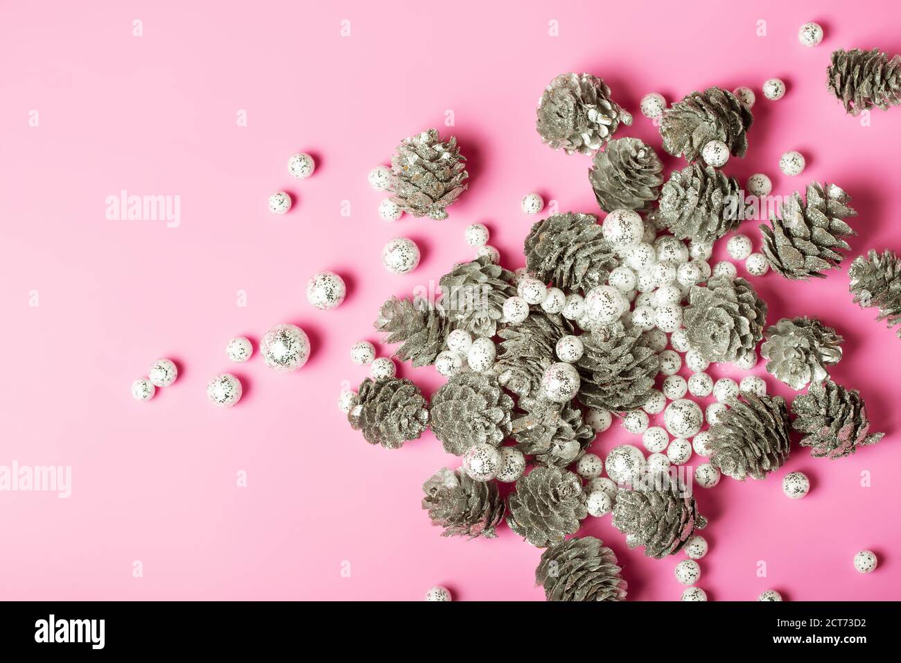 Weihnachtliche festliche Komposition mit silbernen Tannenzapfen und verstreutem Weiß Glitzernde Bälle auf hellrosa Hintergrund Stockfoto