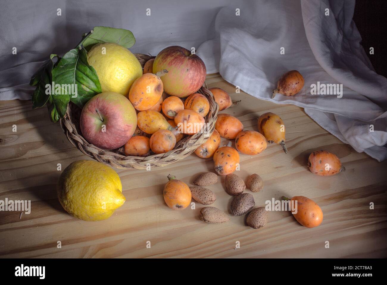 Stillleben in der Ligthmalerei mit einem kleinen Korbkorb mit Früchten, Mispel, Äpfeln, Zitronen und Mandeln in Schale. Stockfoto
