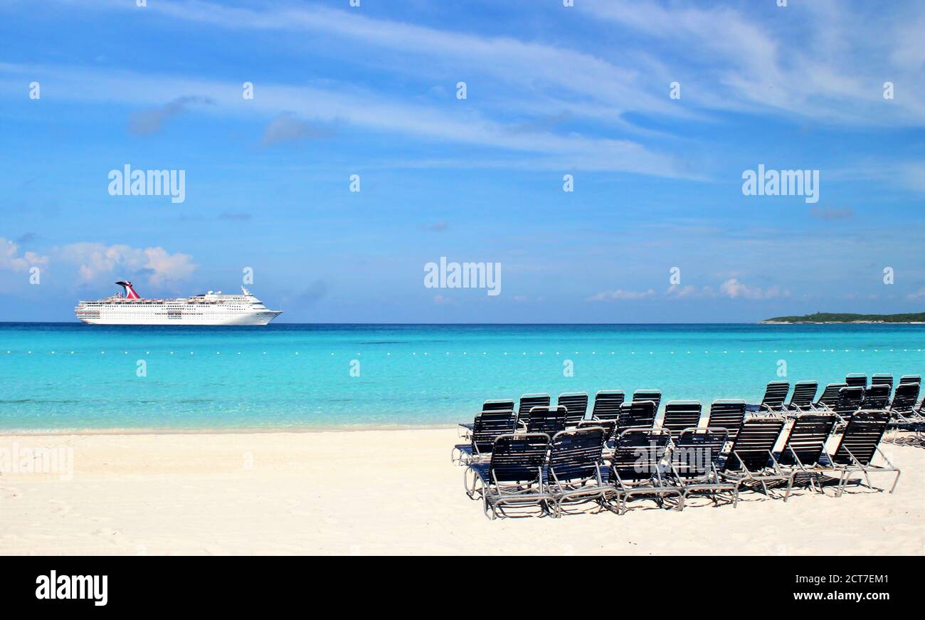 Strandliegen an einer wunderschönen blauen Küste mit einem Das Kreuzfahrtschiff dockte an der Küste an Stockfoto
