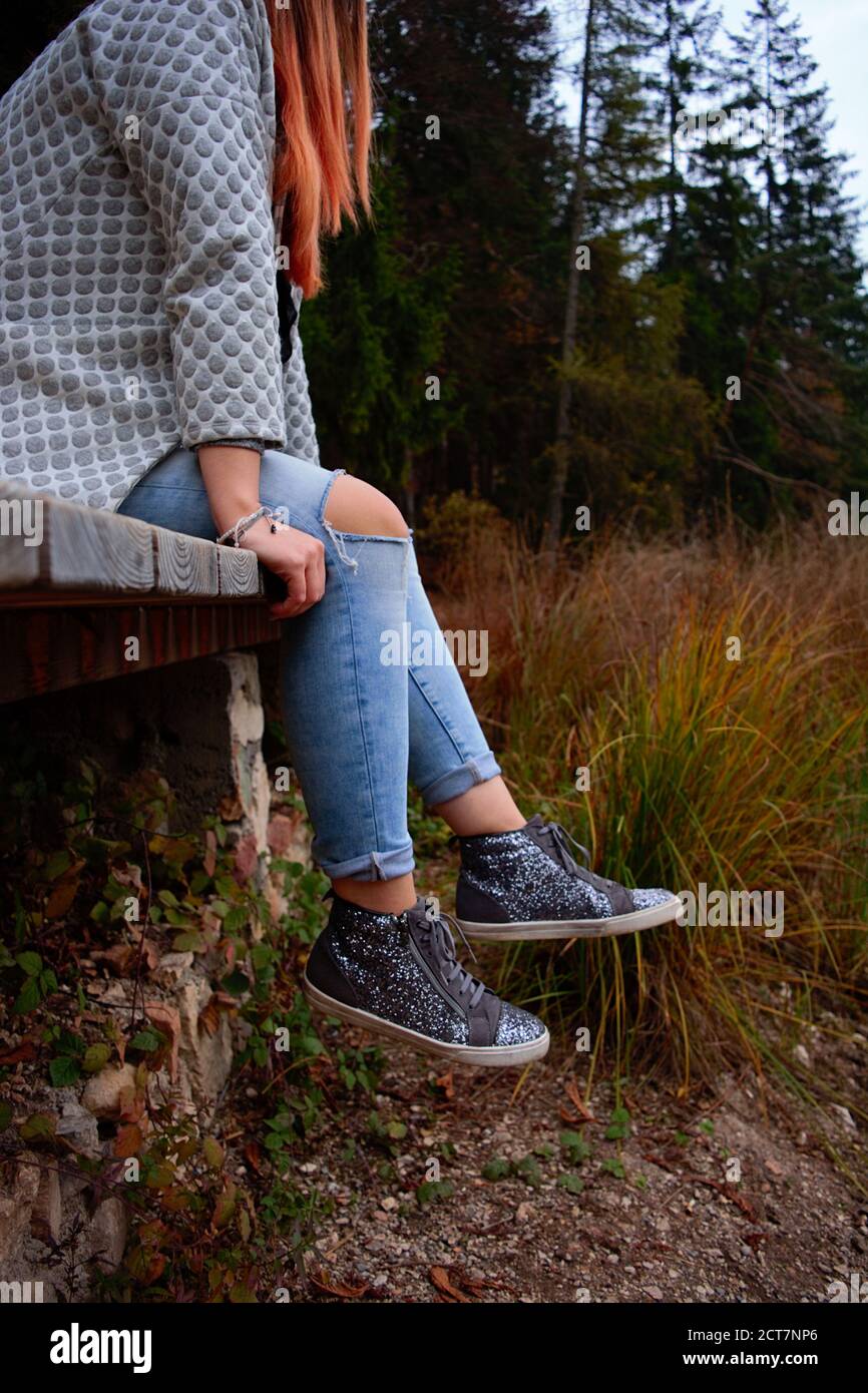 Junge rothaarige Mädchen mit modernem Outfit sitzt in der Nähe herbstliche Landschaft In einem Park Stockfoto