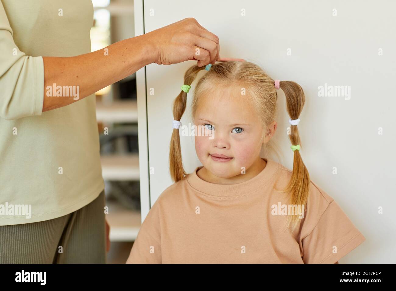 Nahaufnahme von unkenntlich fürsorglichen Mutter Kämmen Haare von niedlichen Mädchen mit Down-Syndrom und binden sie in Zöpfen, kopieren Raum Stockfoto