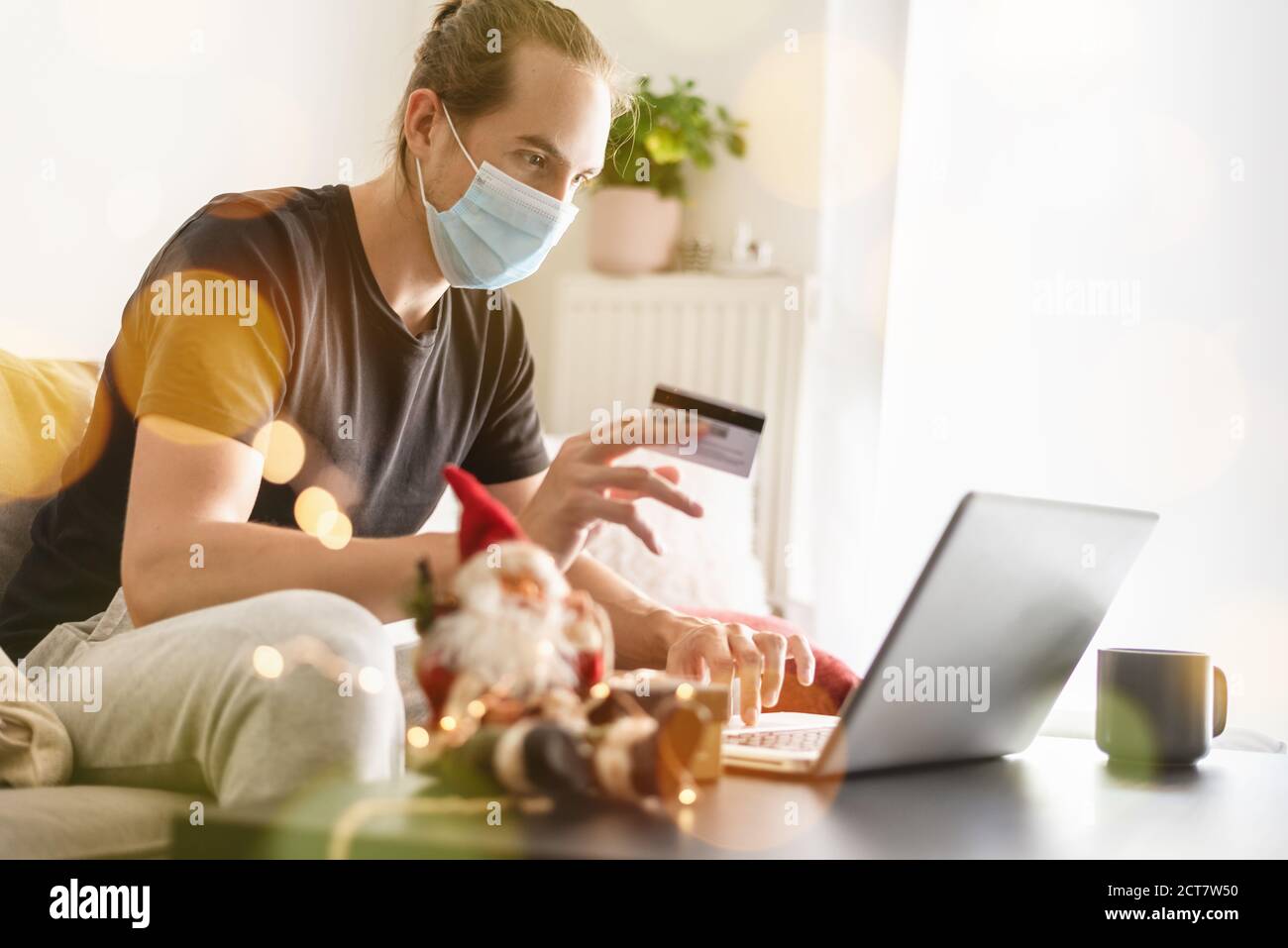 Mann mit Schutzmaske zu Hause einkaufen online mit Kreditkarte für Weihnachten. Stockfoto