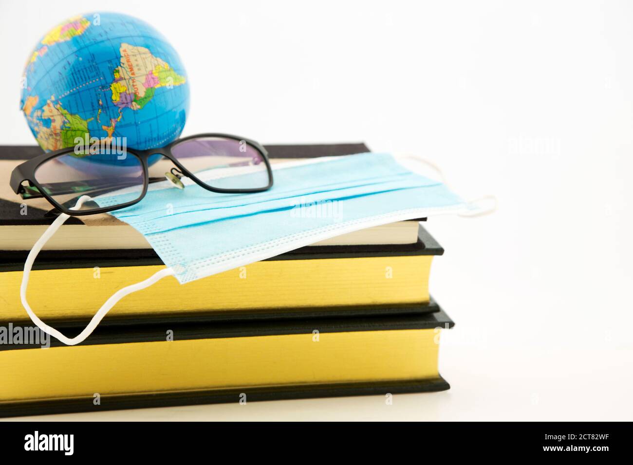 Konzeptuelles Bild globaler Pandemiefragen in Schutzmaske, Büchern, Globus und Brillen, Symbolen der Schule, des Lernens und der vernetzten Forschung Stockfoto