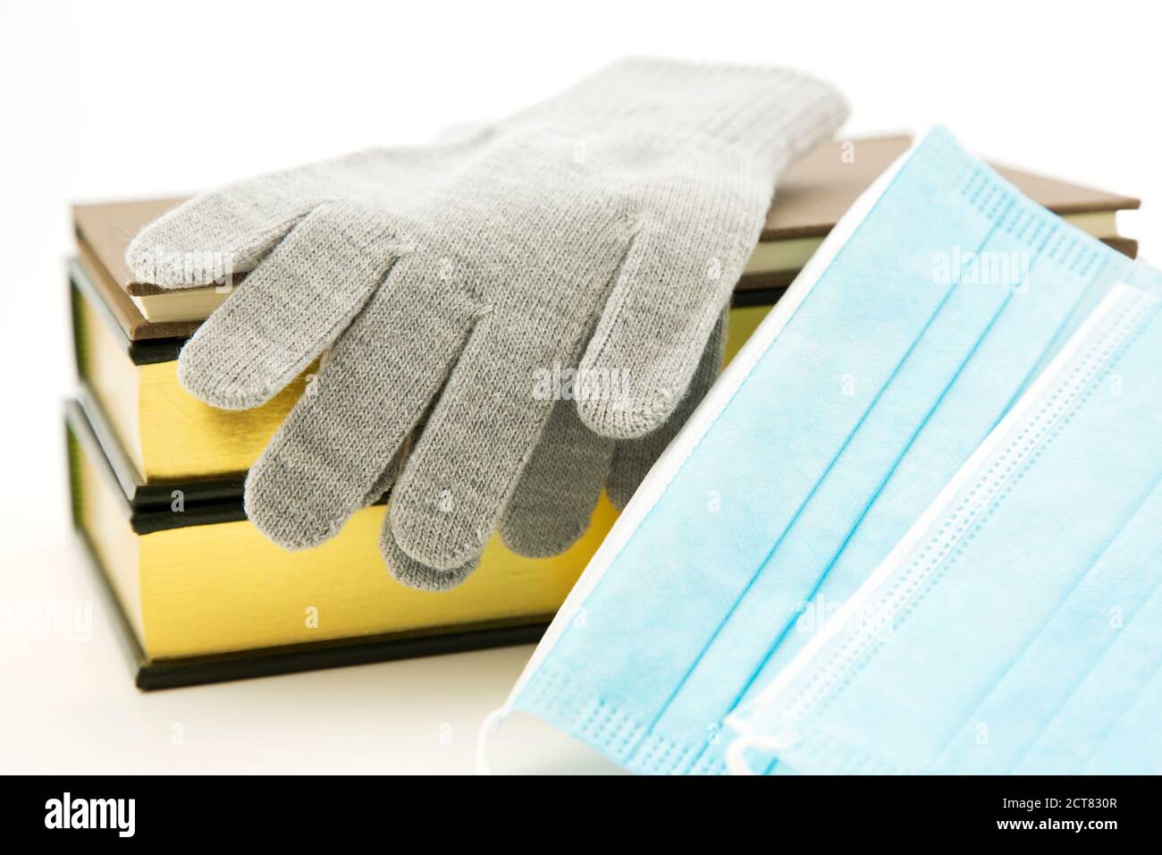 Graue Winterhandschuhe und Bücher, die mit Covid-Masken platziert sind, spiegeln wesentliche persönliche Schutzausrüstung, PSA und Schulausrüstung für die Wintergrippezeit in Corona wider Stockfoto
