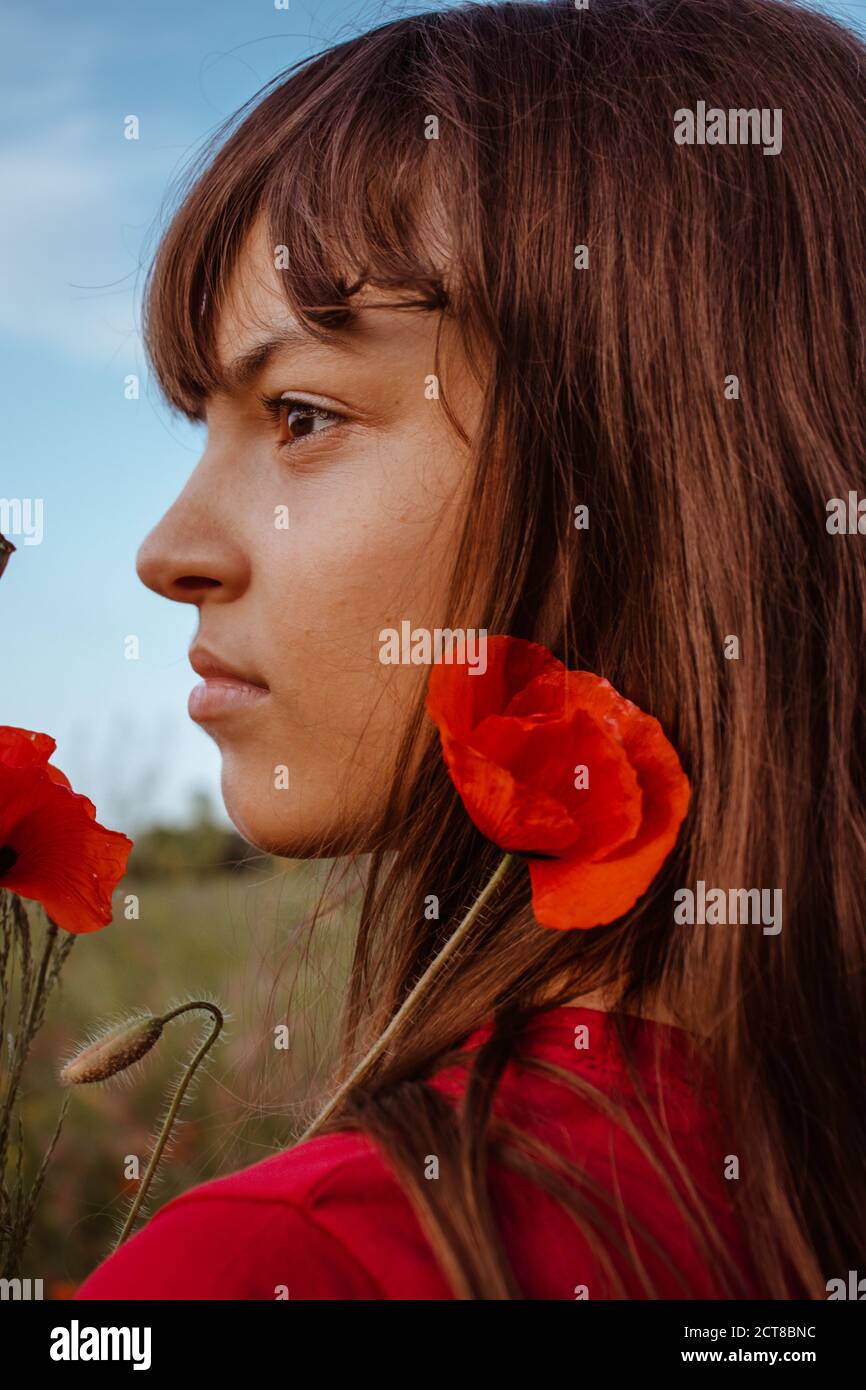 Ein junges weißes Teenager-Mädchen Porträt close-up in profileon Natur Wiese mit rot blühenden Mohnblumen Blumenstrauß Stockfoto