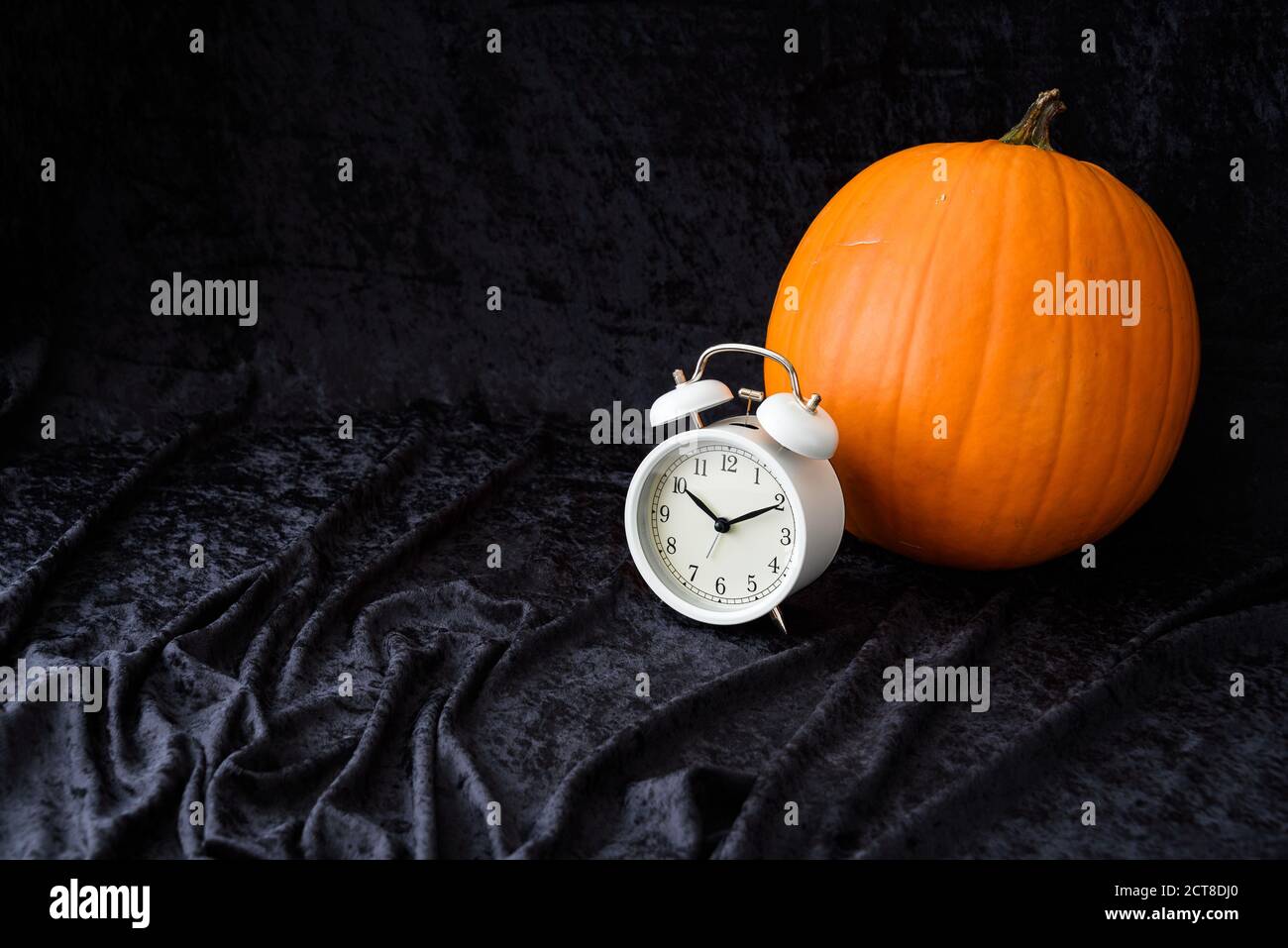 Orangefarbener Kürbis und klassischer weißer Wecker auf schwarzem Samthintergrund, Herbstzeitwechsel Stockfoto