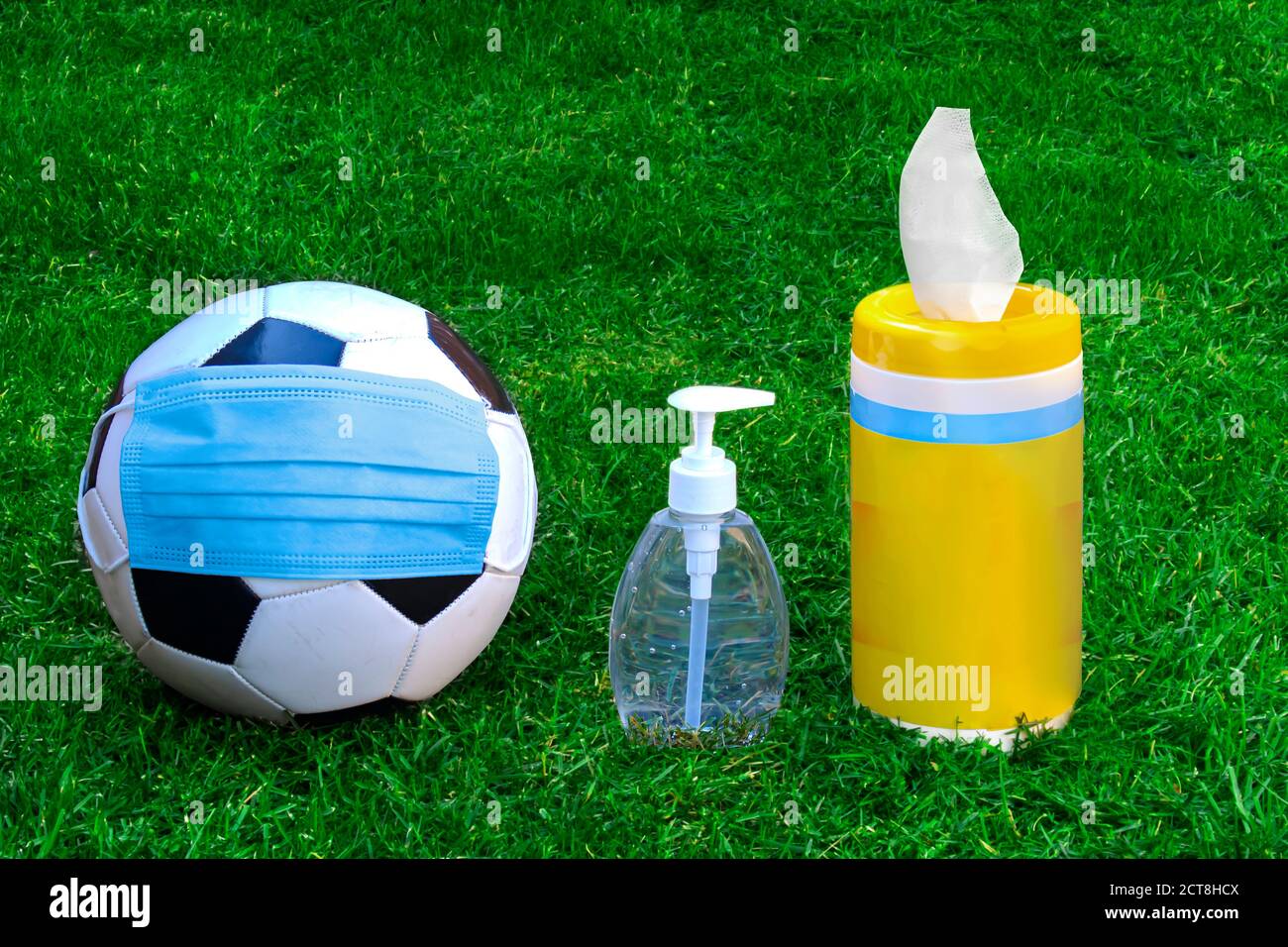 Ein Fußball, Fußball mit Gesichtsmaske, Händedesinfektionsmittel und Desinfektionstücher auf grünem Gras. Konzept Fußball in Pandemie, covid-19 oder cor Stockfoto