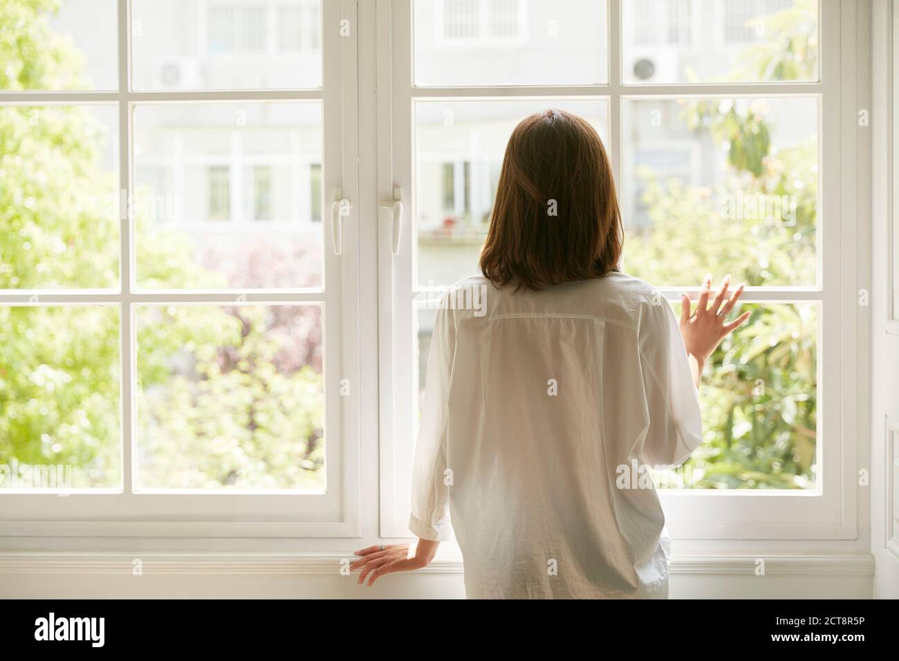 Rückansicht einer jungen asiatischen Frau, die aus schaut Fenster zu Hause Stockfoto