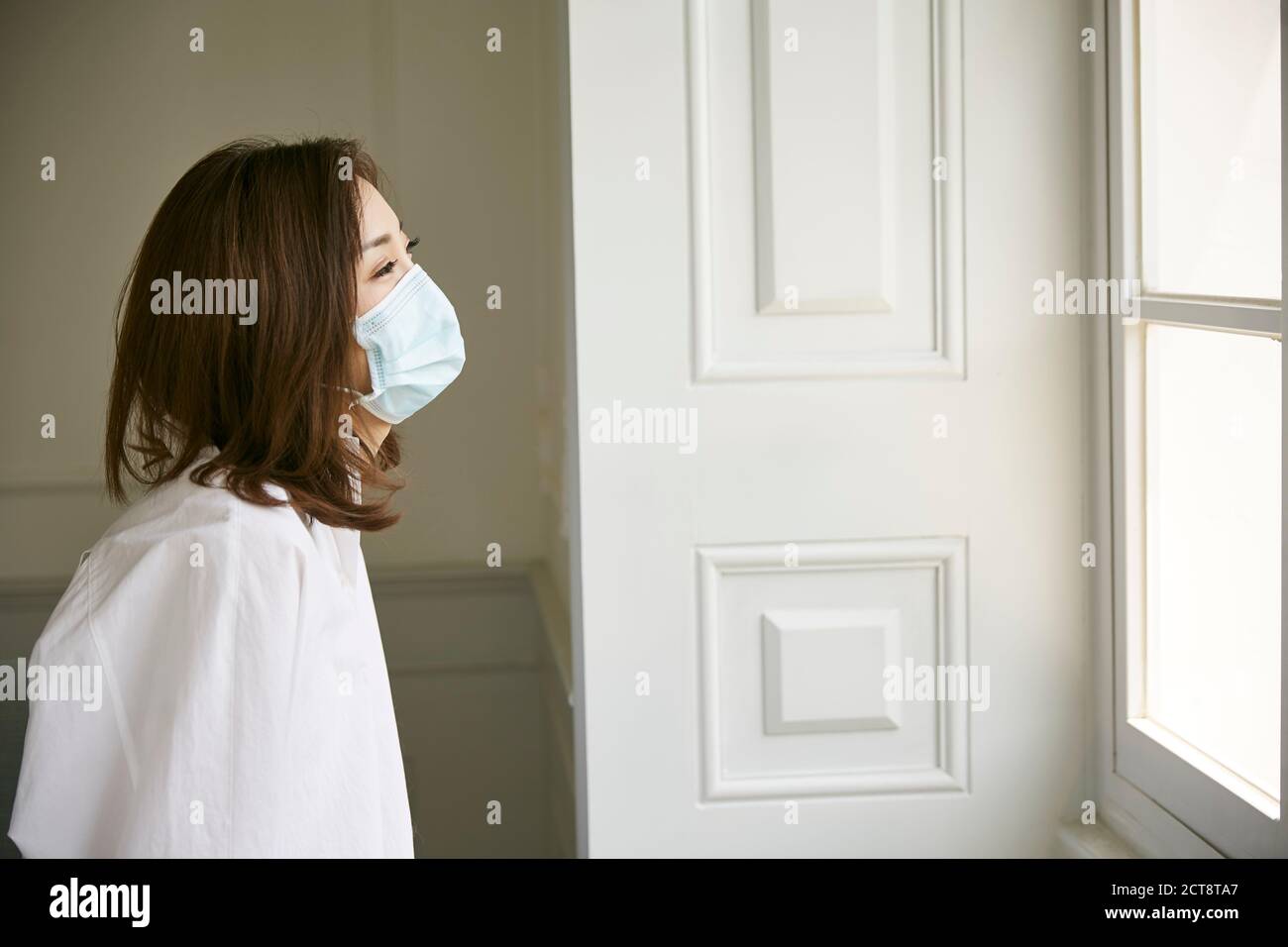 Junge asiatische Frau Quarantäne zu Hause tragen Maske Blick aus Des Fensters Stockfoto