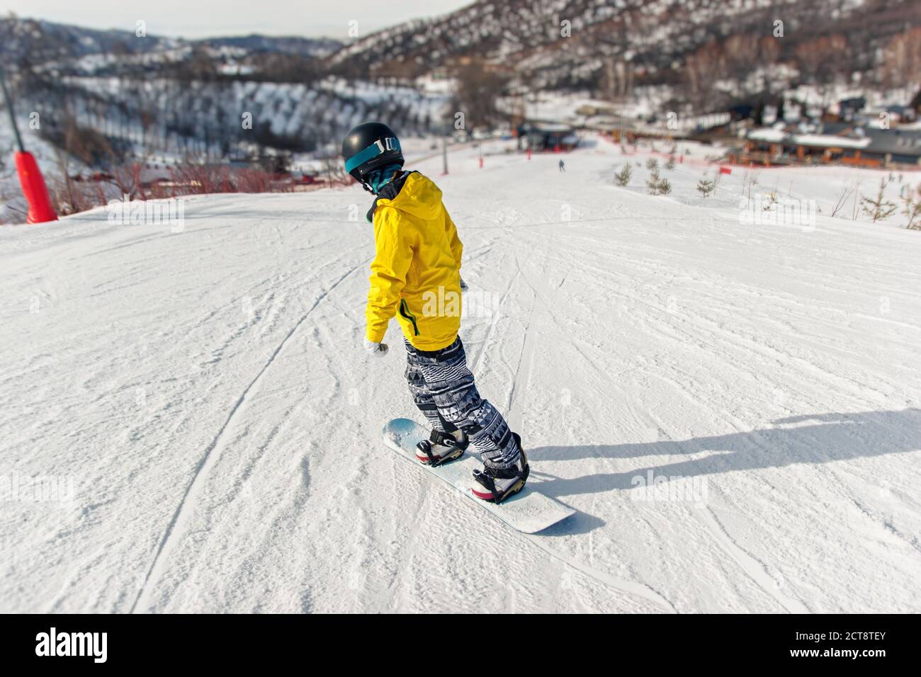 Snowboarder in schwarzem Helm, gelbe Jacke lernt Snowboardtechnik auf der Skipiste Stockfoto