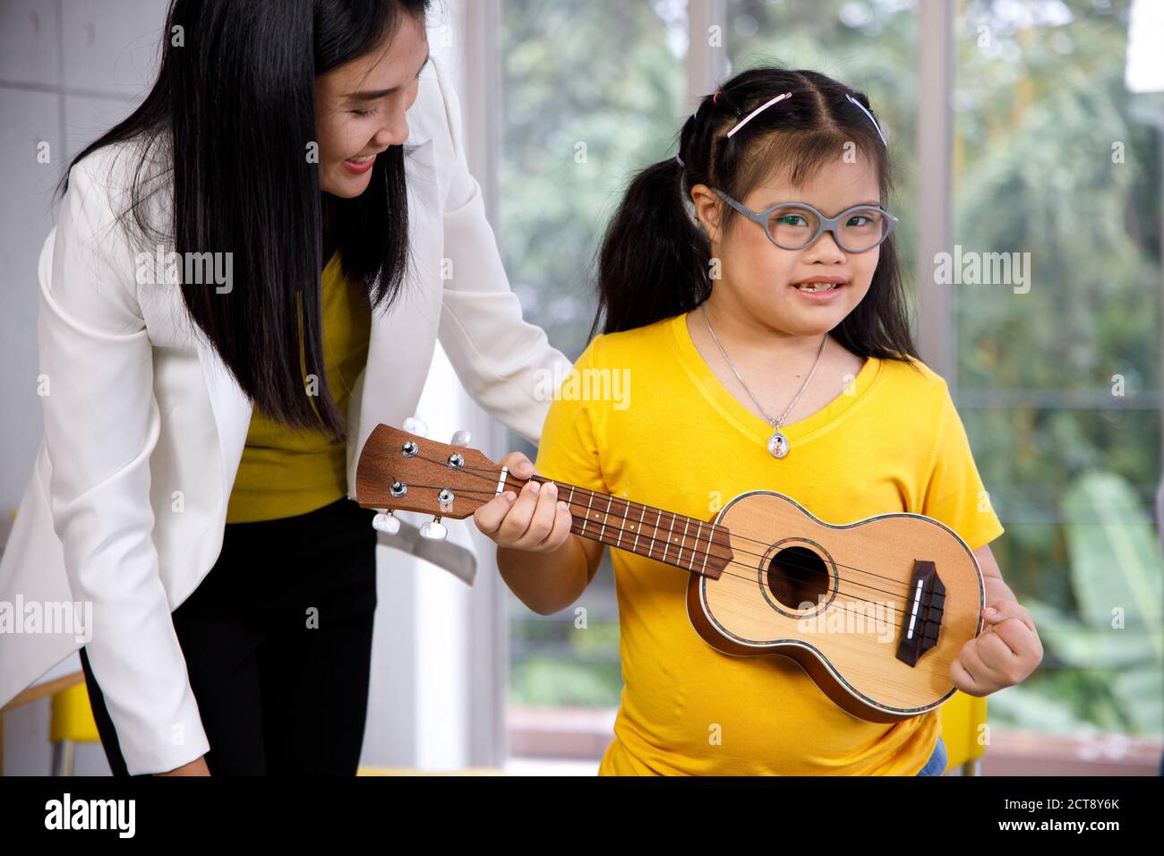 Asiatische Lehrer lehren Ukulele Mädchen mit Down-Syndrom. Konzept behindertes Kind lernen in der Schule. Stockfoto