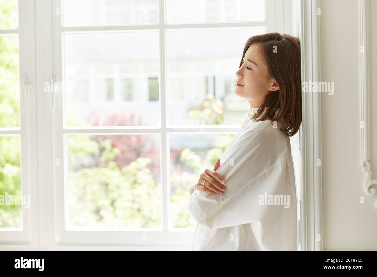 Schöne junge asiatische Frau am Fenster zu Hause Arme stehen Gekreuzte Augen geschlossen Stockfoto