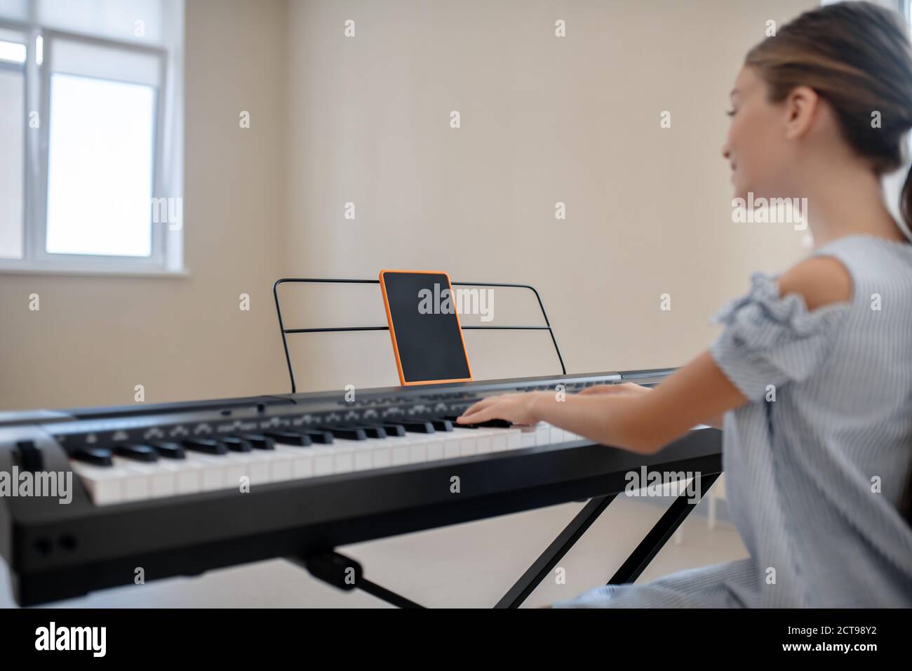 Langhaarige Mädchen in blauem Kleid sitzt am Synthesizer und Sport Stockfoto