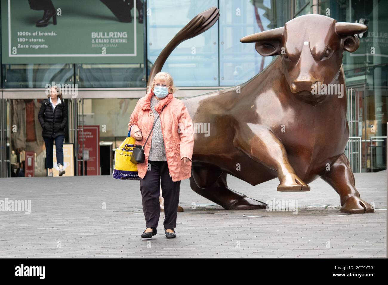 Bild aufgenommen am Tag der Einführung von Coronavirus-Einschränkungen in Birmingham. Eine Frau geht vor dem Stier im Bullring Einkaufszentrum und trägt eine Gesichtsbedeckung. Stockfoto