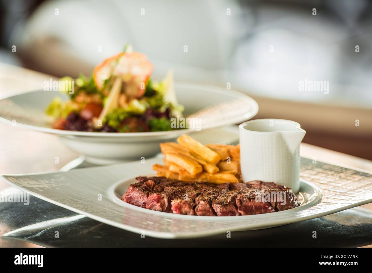 Medium rare Steak mit Pommes Frites und gemischter Salat im Hintergrund Stockfoto