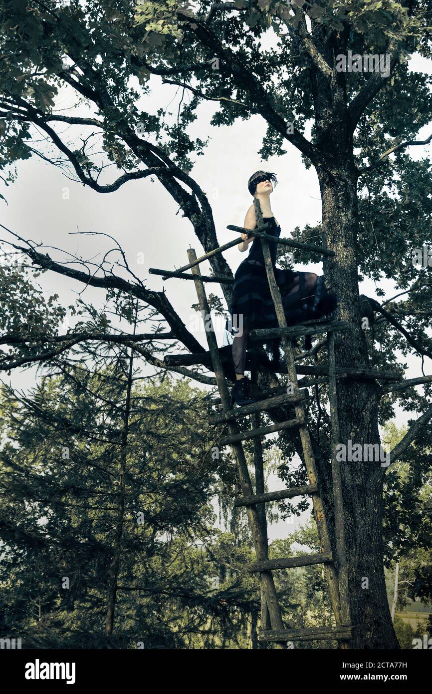 Deutschland, Blindfolded Frau auf Ansitz in Baum Stockfoto