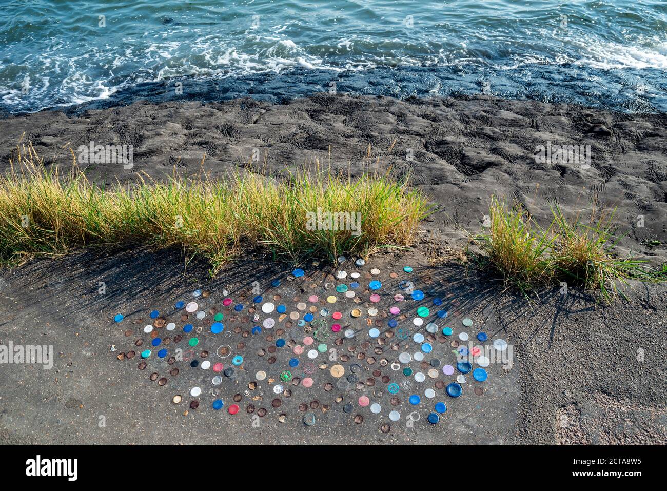 Plastikflaschen-Tops wurden in Chalkwell, Southend on Sea, Essex, Großbritannien, in die Teerschicht der Ufermauer geschoben. Schlackenweg an der Themse Mündung mit Flaschenverschlüssen Stockfoto