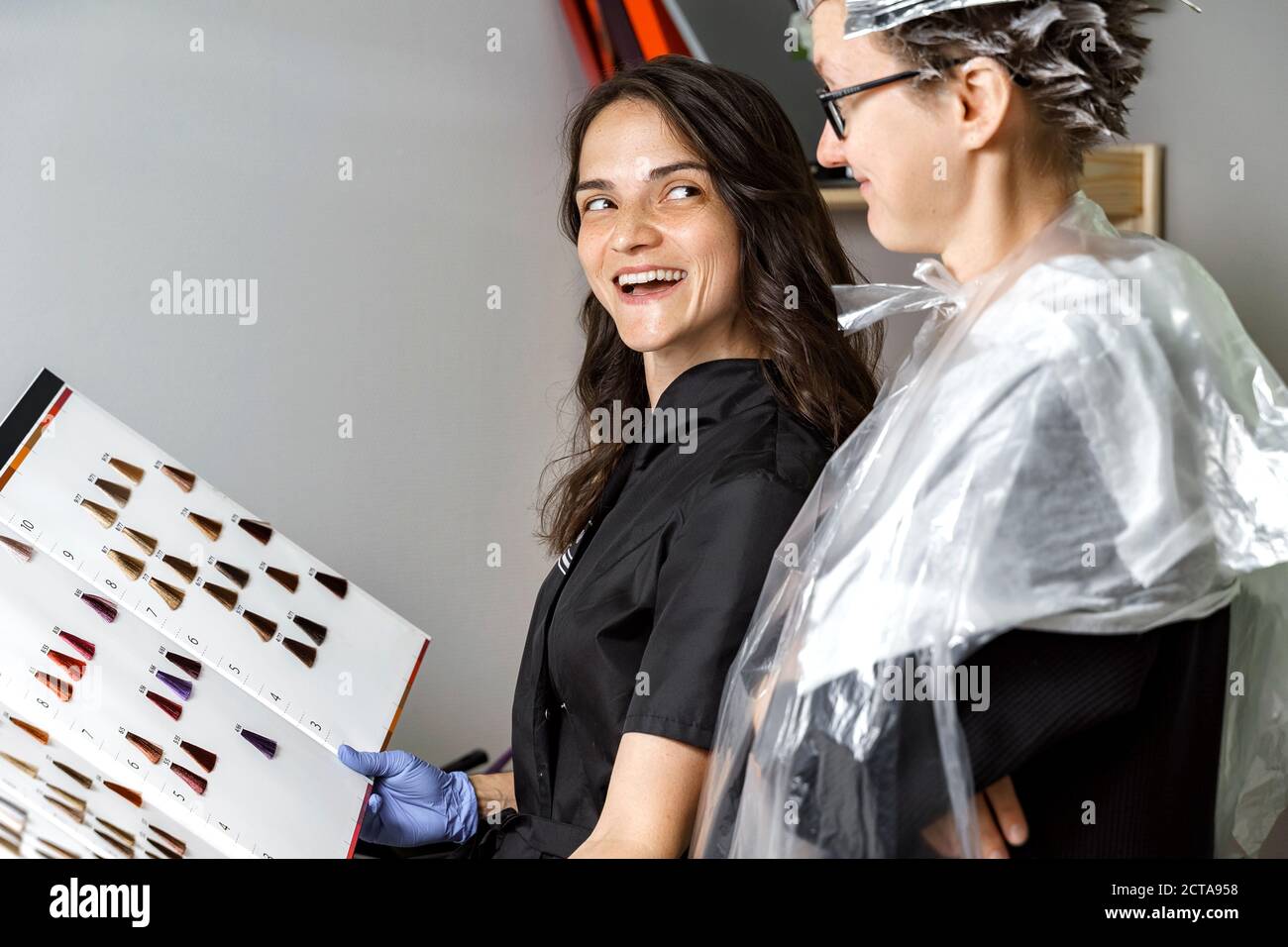 Lächelnde junge Frau und Friseur Wahl Haarfarbe aus Palette vor dem Färben im Schönheitssalon. Schönheit, Haarfärbung und Menschen Konzept Stockfoto