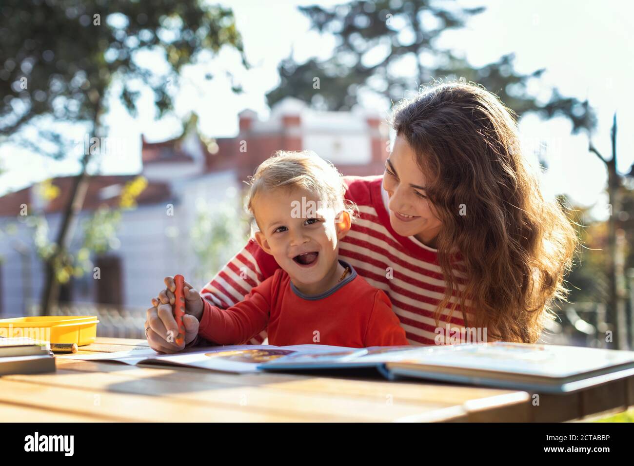 Mutter und Sohn zeichnen im Garten auf dem Picknicktisch, Sohn schaut auf die Kamera Stockfoto